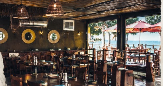 The finished dining room at 40 Knots: dark timber tables laid for service, woven lamps, portholes on the wall and the terrace beyond