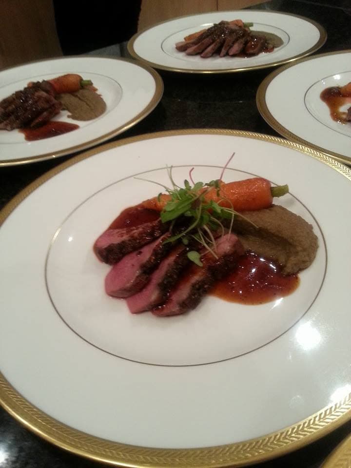 Sliced duck breast with a baby carrot, purée and jus on gold-rimmed china