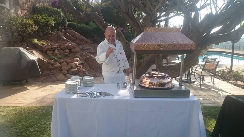Paul in whites at a carving station beneath the trees in the residence garden, the table laid in white linen