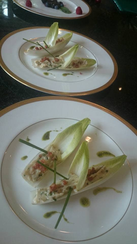 Endive leaves filled with a light salad, dressed with herb oil, on gold-rimmed china