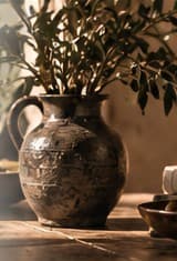 A clay jug with an olive branch and a bowl of olives on a wooden table in warm light