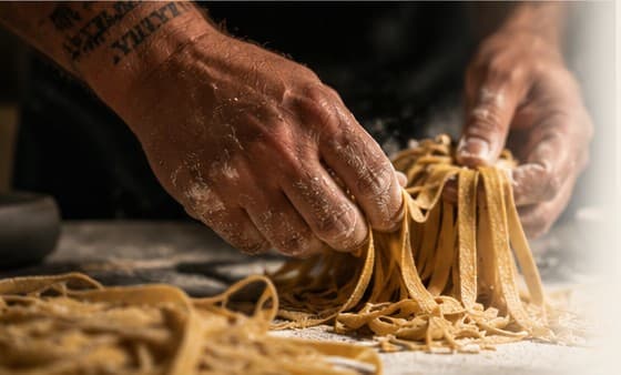 Floured hands lifting fresh tagliatelle from a wooden board