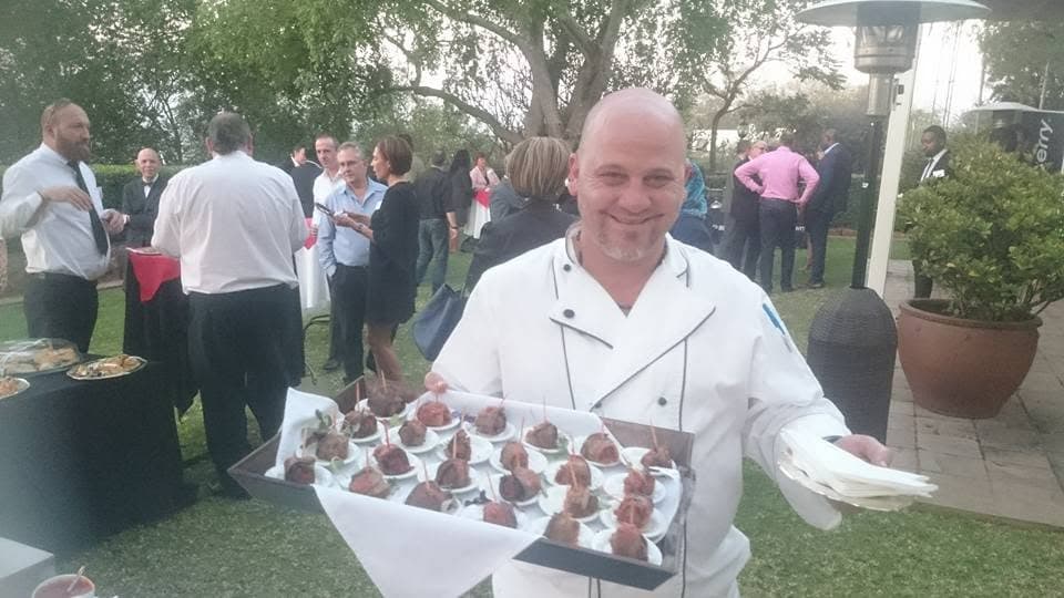 Paul in whites carrying a tray of canapés through a garden reception