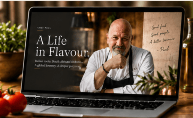 A laptop on a kitchen counter showing Chef Paul on screen, tomatoes and olive oil beside it