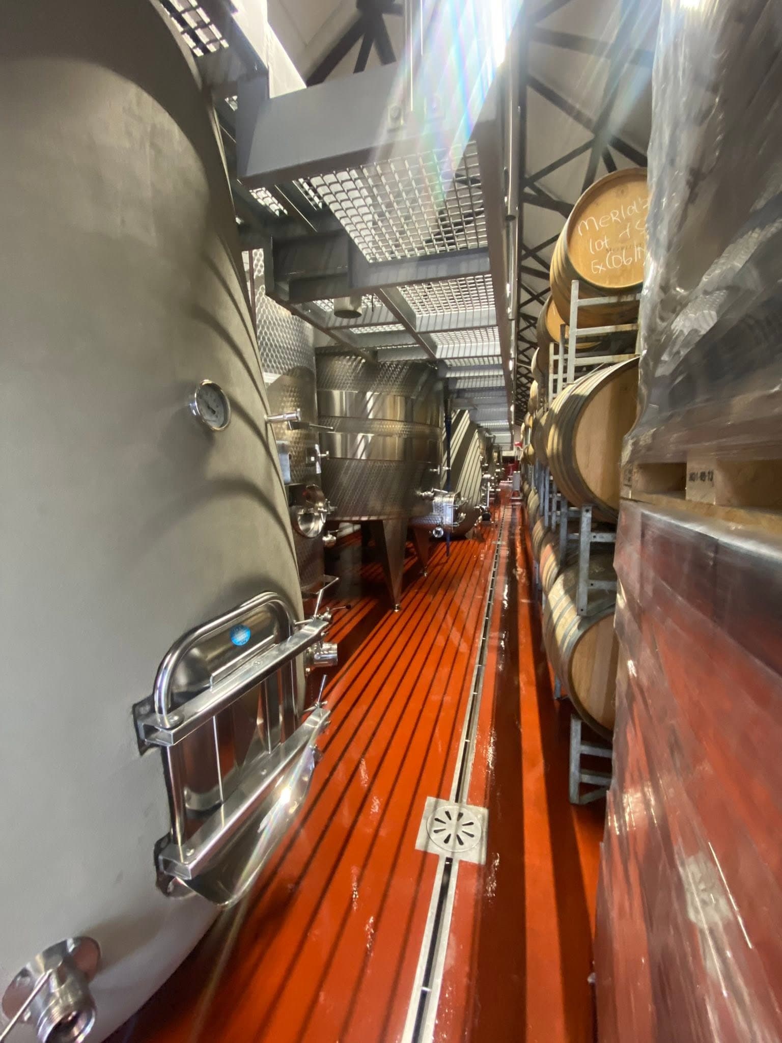 Barrels racked along a red cellar floor between steel tanks