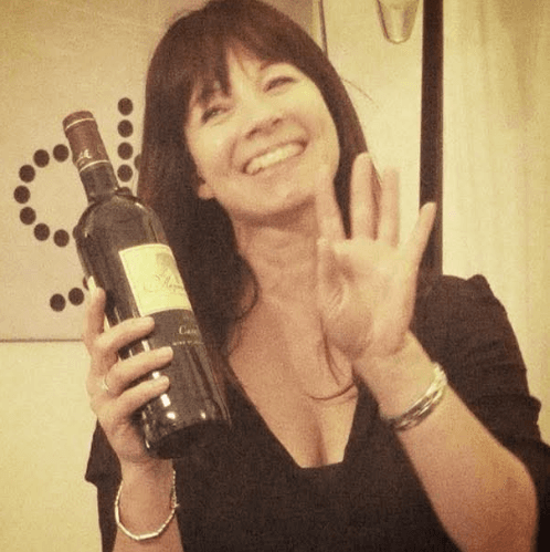 Christelle, laughing, holding up a bottle of red wine