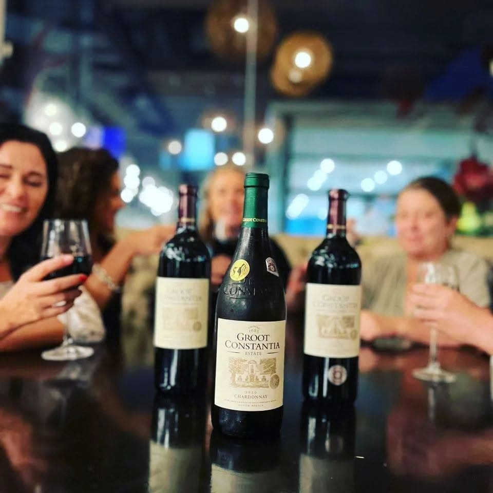 Friends raising glasses behind a row of bottles at a tasting