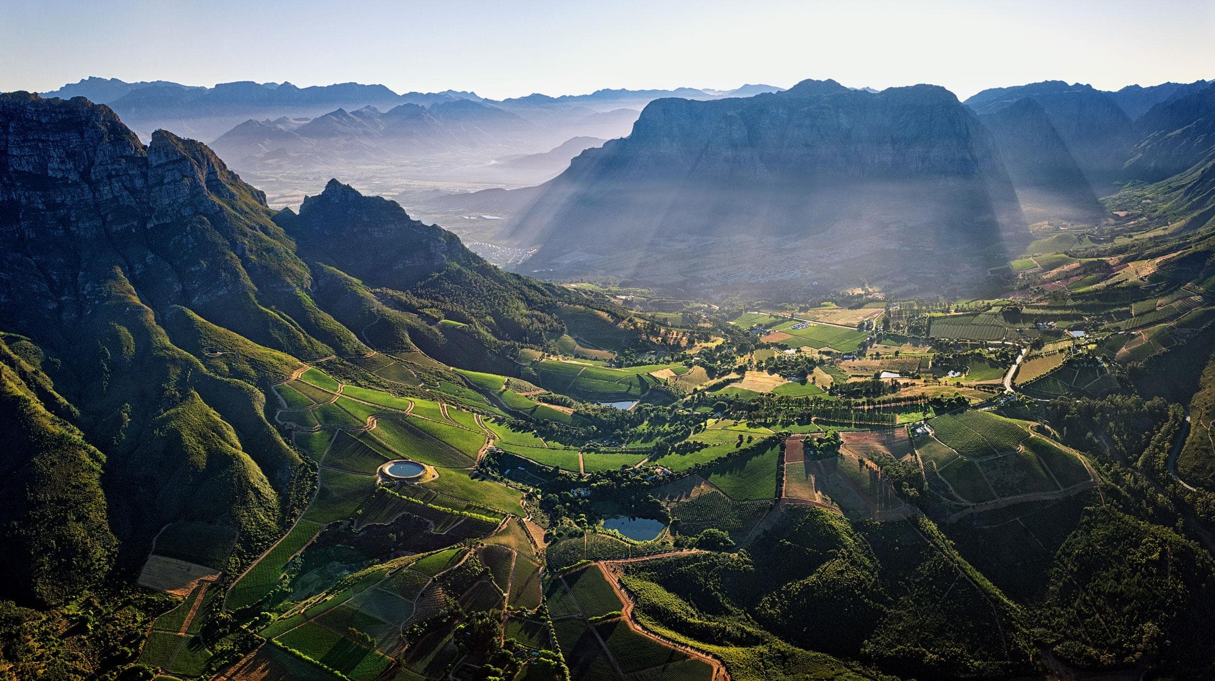The Stellenbosch winelands from the air: vineyards in a green valley below the Simonsberg, morning light through the haze